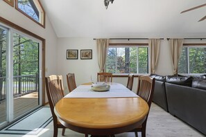 Comedor con mesa de madera, sillas y vista al exterior a través de amplios ventanales.