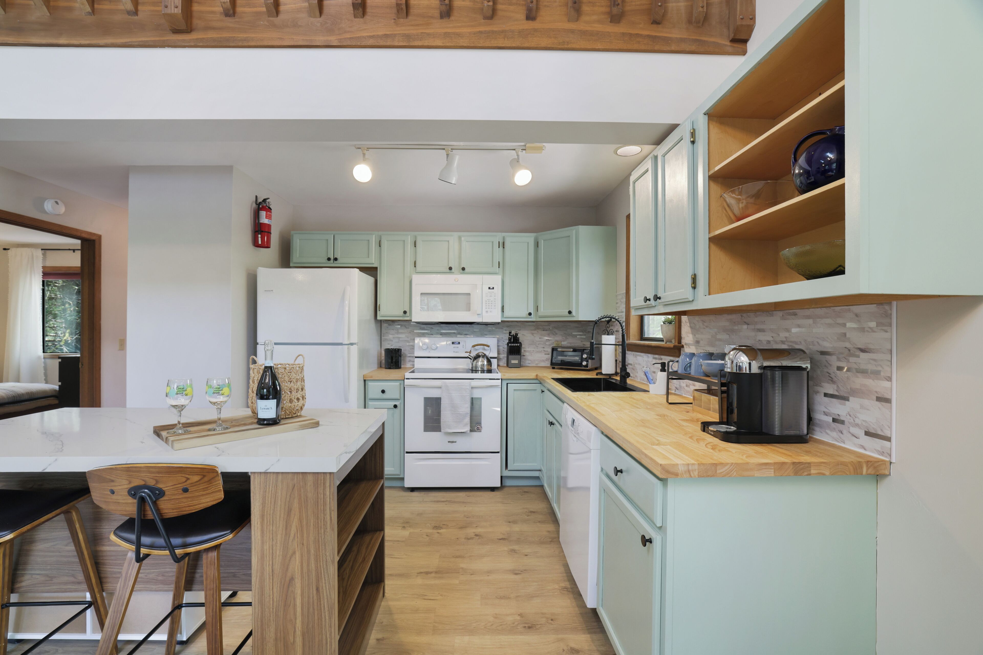 A kitchen with a central island, wooden chairs, a microwave, a stove, and a coffee maker.