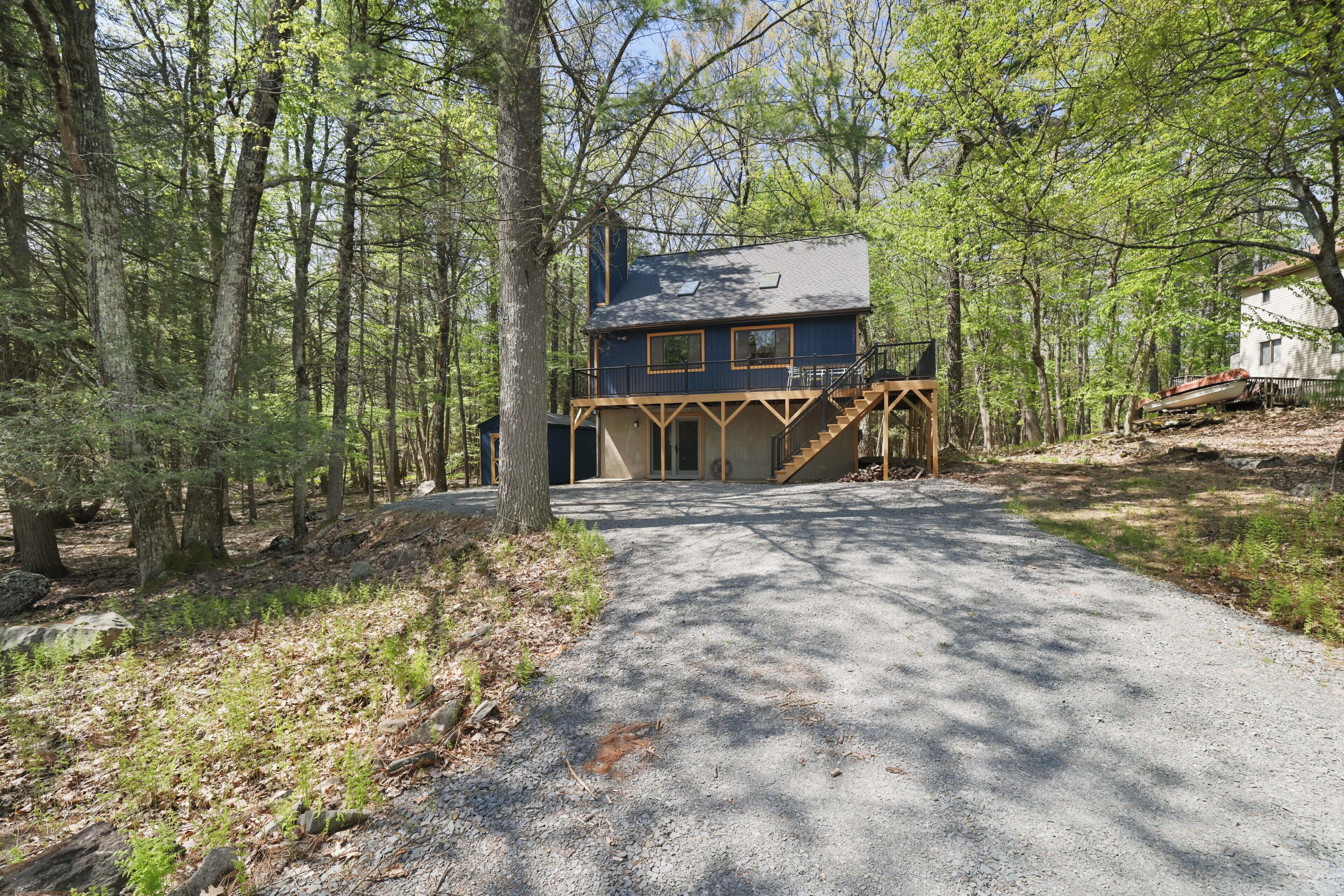 A cabin with a gravel driveway, surrounded by trees.