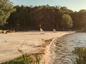 Una playa arenosa con una bandera, árboles y un banco.