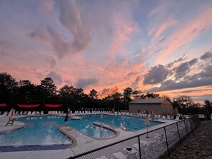 Una piscina con varias pistas de natación, rodeada de sillas de descanso y sombrillas, bajo un cielo al atardecer.