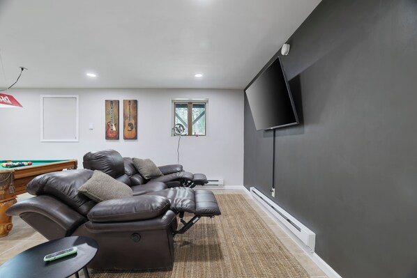 Una sala de estar moderna con un sofá reclinable, una mesa de billar y un televisor de pantalla plana montado en la pared.