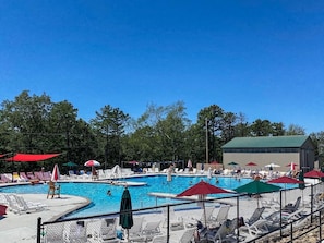 Piscina con sillas de descanso y sombrillas, rodeada por una valla.
