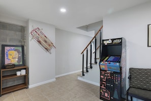 Una sala de estar con una escalera de madera, una consola de videojuegos y una obra de arte enmarcada en la pared.