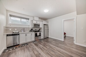 A modern kitchen with white cabinets, stainless steel appliances, and a wooden floor. - Luxurious Basement: Hidden Oasis (Edmonton)