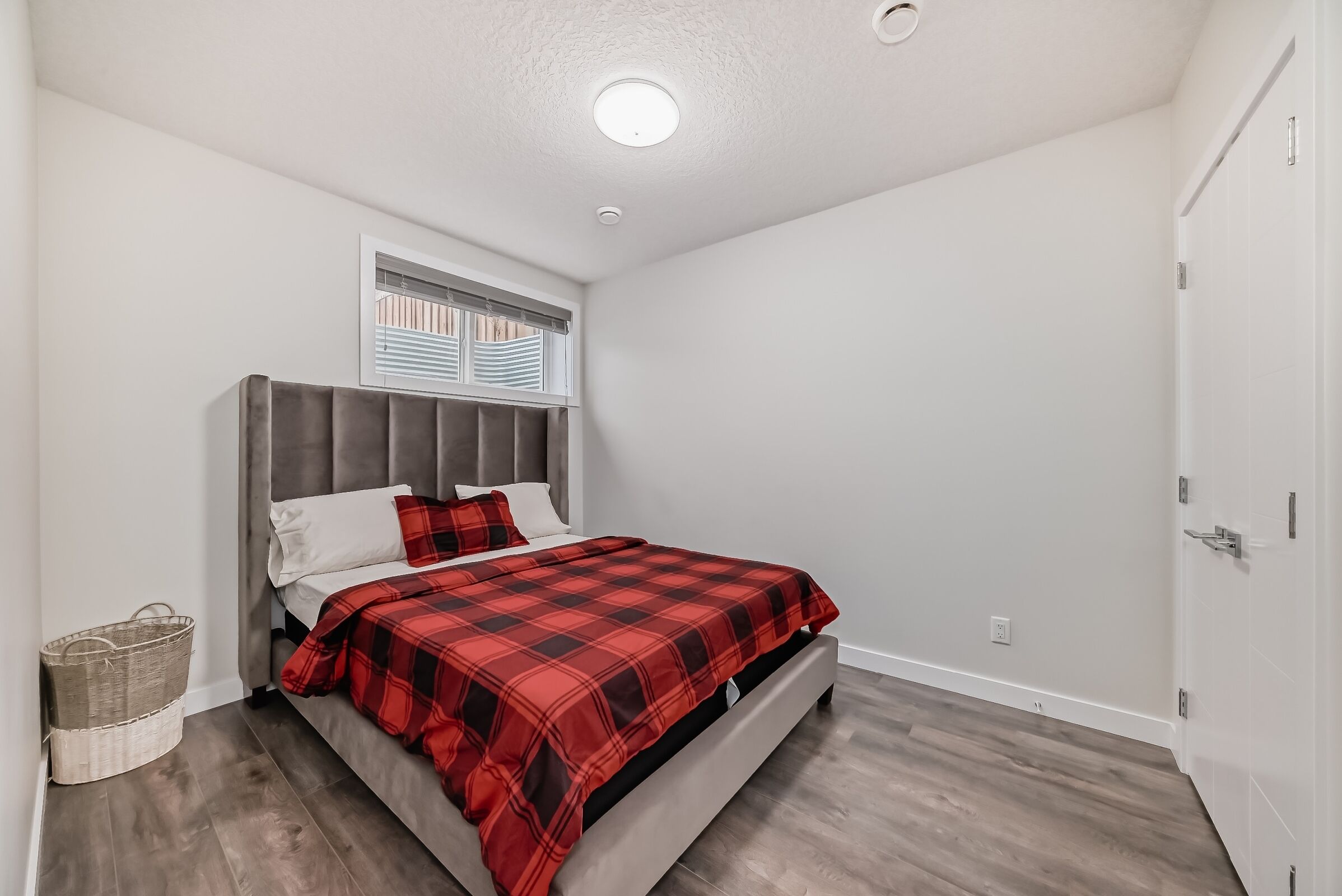 Een slaapkamer met een bed, een raam, een plafondlamp en een deur.