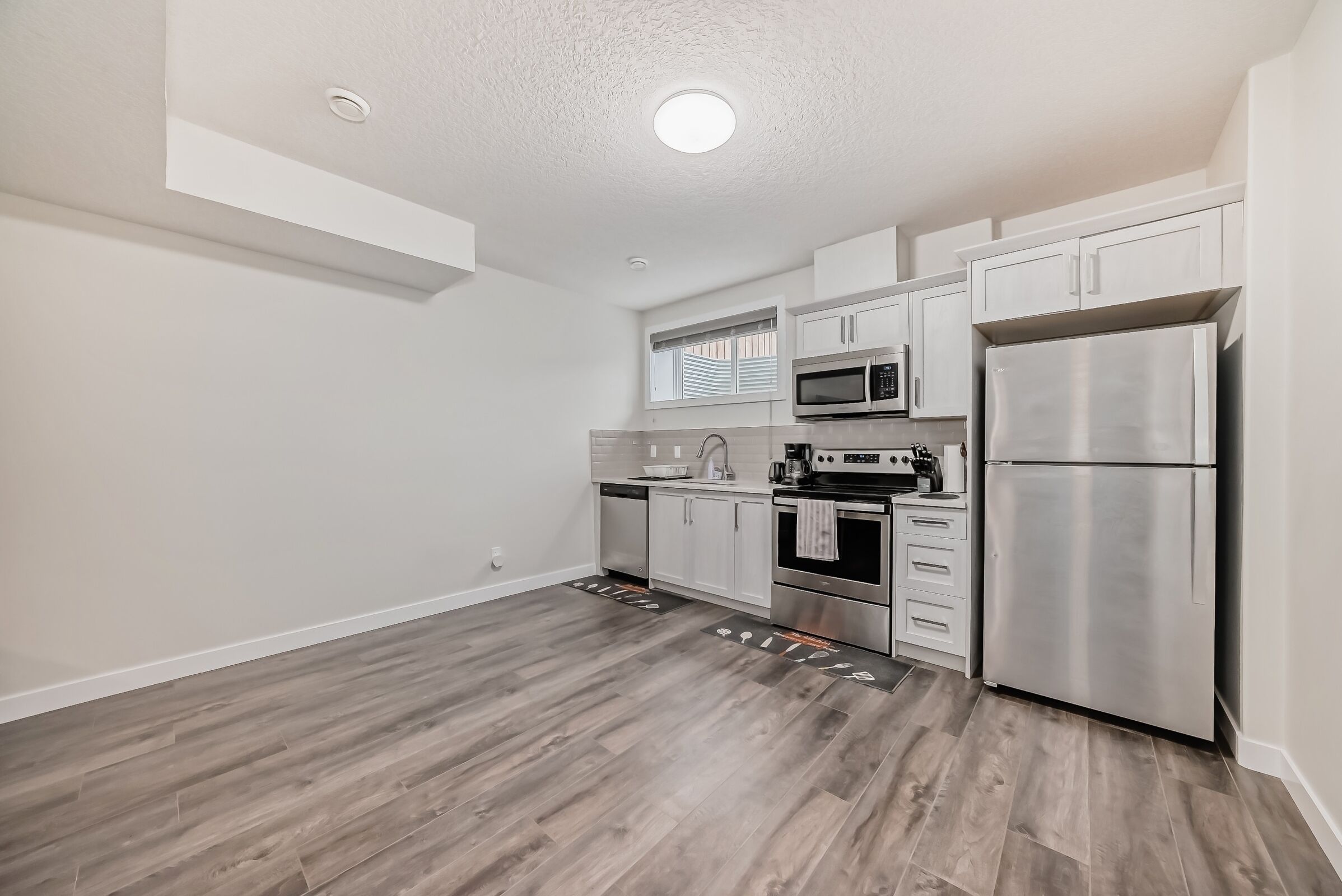 A modern kitchen with white cabinets, stainless steel appliances, and a wooden floor.