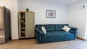 Ein modernes Wohnzimmer mit einem türkisfarbenen Sofa, einer eingebauten Garderobe und einem gerahmten Bild an der Wand.