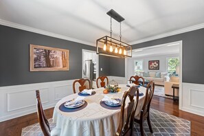 A dining room with a round table set for six, a chandelier, and a framed picture on the wall.
