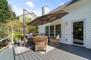 A deck with wicker furniture, a patio umbrella, and a white house in the background.