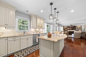 Une cuisine spacieuse avec des meubles blancs, un grand îlot central et des luminaires suspendus.