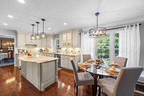 Une cuisine moderne dotée d’un grand îlot central, de luminaires suspendus et d’un coin repas avec une table en verre.