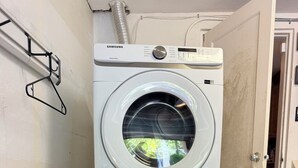 A stacked washer and dryer unit with a control panel, a door with a key lock, and a metal rack on the wall. - Rio Vista Gem , Walk to Las Olas , 6 Min to Beach ,Private Backyard 2 Bedrooms (Fort Lauderdale)