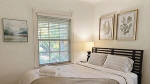 A bedroom with a bed, a window with blinds, a bedside lamp, and framed botanical prints on the wall. - Rio Vista Gem , Walk to Las Olas , 6 Min to Beach ,Private Backyard 2 Bedrooms (Fort Lauderdale)