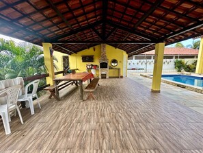 Eine Terrass mit Backofen, Pool und überdachter Sitzgruppe.