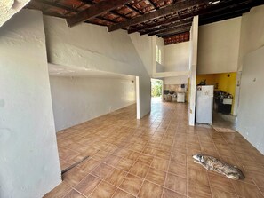 A spacious interior with a tiled floor, a dog lying on the floor, and a kitchen area visible in the background. - Beach house with pool in Porto das Dunas, 7 bedrooms + garage for 6 cars. (Aquiraz)