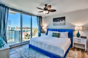 Ein Schlafzimmer mit einem großen Bett, einem Deckenventilator, einem Nachttisch mit Lampe und Blick auf Stadt und Wasser.
