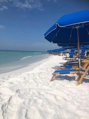 A beach with rows of blue umbrellas and wooden lounge chairs. - Destin’d to Unwind | Walk to Beach | Gulf Views (Destin)