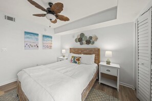 A bedroom with a bed, two bedside tables, a ceiling fan, artwork on the wall, and a wooden floor. - Destin’d to Unwind | Walk to Beach | Gulf Views (Destin)