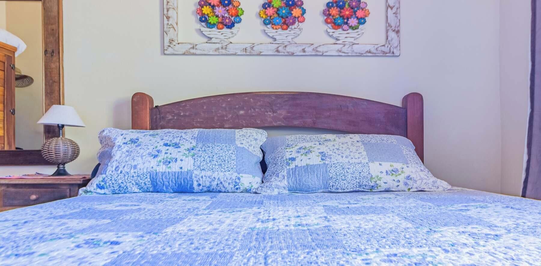 A bed with a floral-patterned bedspread and two pillows, a wooden headboard, a bedside lamp, and a wall-mounted floral artwork.