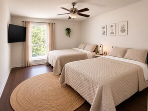 A bedroom with two beds, a ceiling fan, a TV, and a window with curtains. - Windmill Retreat - Modern Farmhouse - Game Room - Sleeps 10 - 1 acre (Brenham)