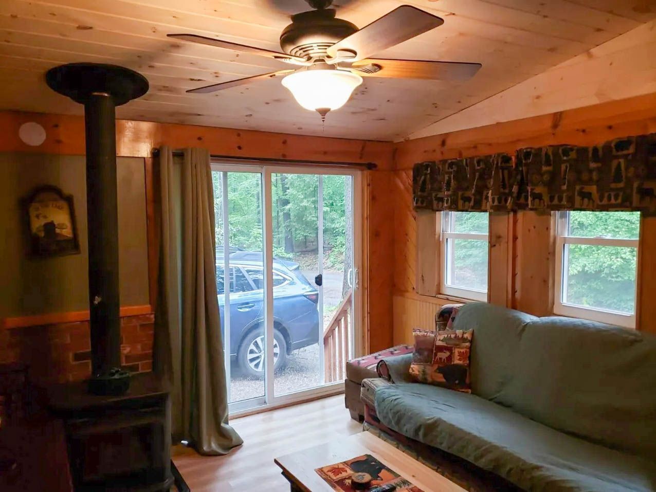 A cozy cabin interior with a sofa, a fireplace, and a ceiling fan.