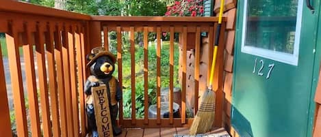 A wooden deck with a bear holding a sign, a broom, and a green door with the number 127.