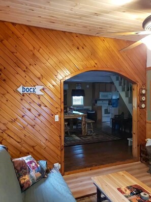 Interior de madera con un letrero que indica un muelle, un sofá, una mesa de centro y una cocina al fondo.
