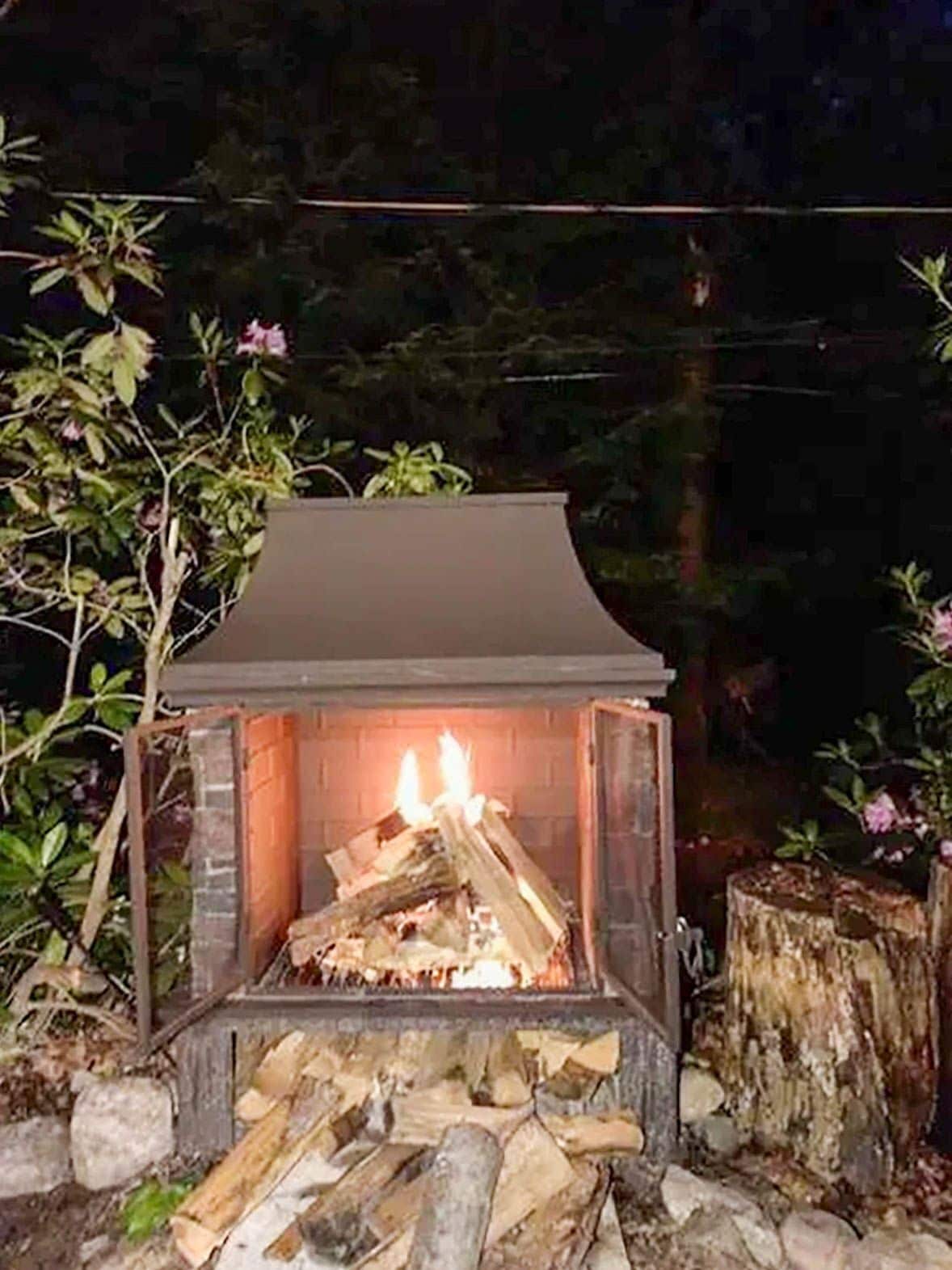 Una chimenea con leña, rodeada de plantas y un muro de ladrillo.