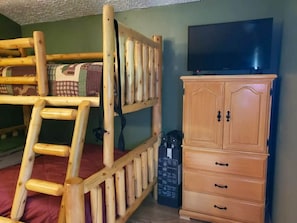 Kerrossänky, jossa on tikkaat, jalustalla oleva televisio ja puinen kaappi.