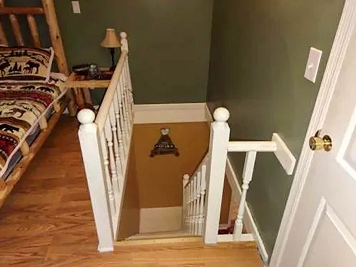 A staircase with white balusters and a wooden handrail, leading to a room with a green wall and a patterned rug.
