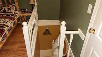 A staircase with white balusters and a wooden handrail, leading to a room with a green wall and a patterned rug.