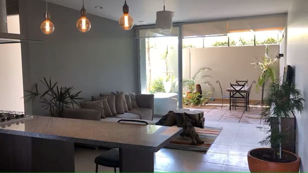Une cuisine moderne dotée d’un îlot central, d’un coin repas avec une table et des chaises, et d’une grande porte-fenêtre coulissante donnant sur une terrasse extérieure.