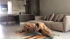 Un salon moderne avec un grand canapé, une table basse en bois et un coin cuisine à l’arrière-plan.