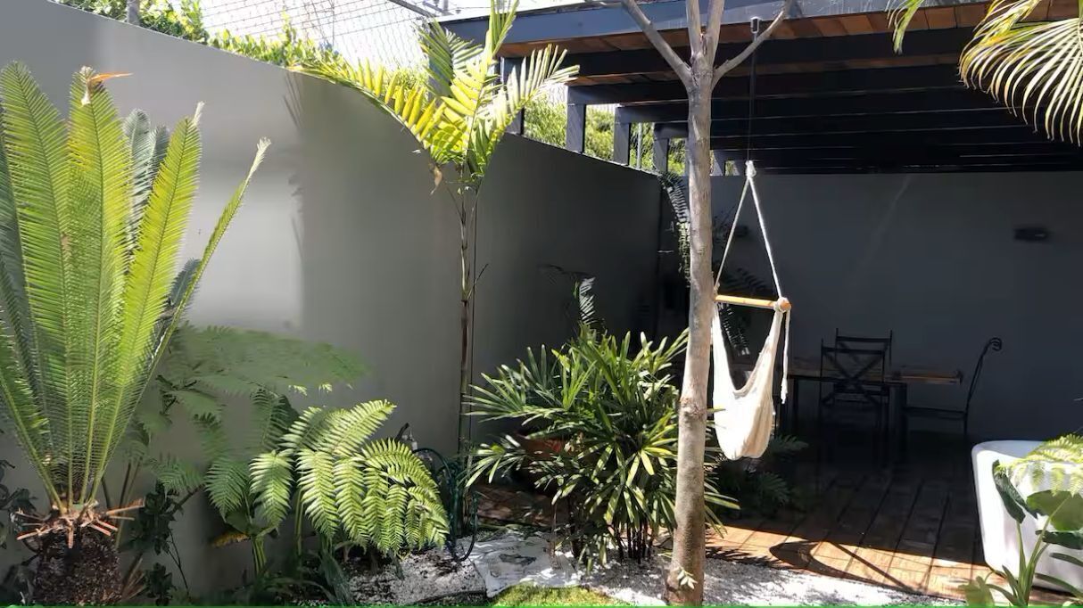 Un jardin agrémenté de diverses plantes, un hamac et un espace patio avec une table et des chaises.