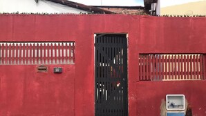 Un mur rouge avec un portail noir, une boîte de branchement bleue et un cône métallique.