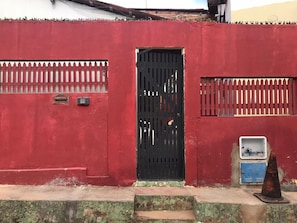 Un mur rouge avec un portail noir, une boîte de branchement bleue et un cône métallique.