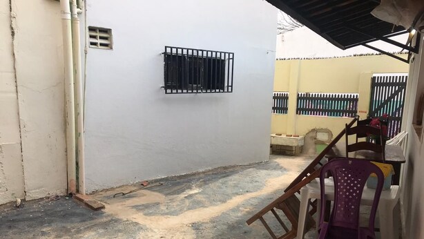 Une cour avec un mur blanc, une fenêtre grillagée et une chaise.