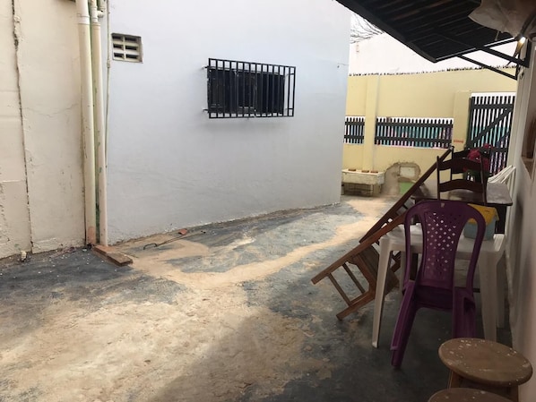 Une cour avec un mur blanc, une fenêtre grillagée et une chaise.