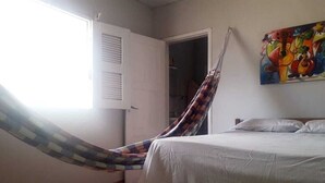 Une pièce avec un lit, un hamac, une porte et un tableau au mur.