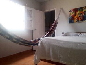 A room with a bed, a hammock, a door, and a painting on the wall.