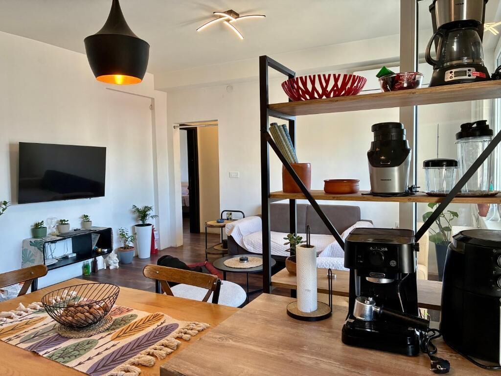 A modern living room with a TV, coffee maker, and a dining area with a table and chairs.