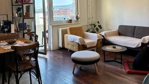 Een woonkamer met een eettafel, stoelen, een bank, een klein voetenbankje, een bijzettafeltje, een plafondventilator en uitzicht door een glazen deur.
