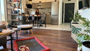 A modern living room with a red cushioned area rug, a dining table with chairs, and a kitchen in the background.