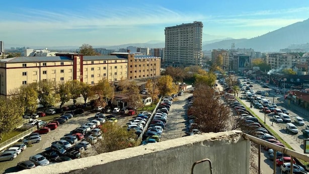 A parking lot with multiple rows of cars, a large building with a flat roof, and a mountain in the background.