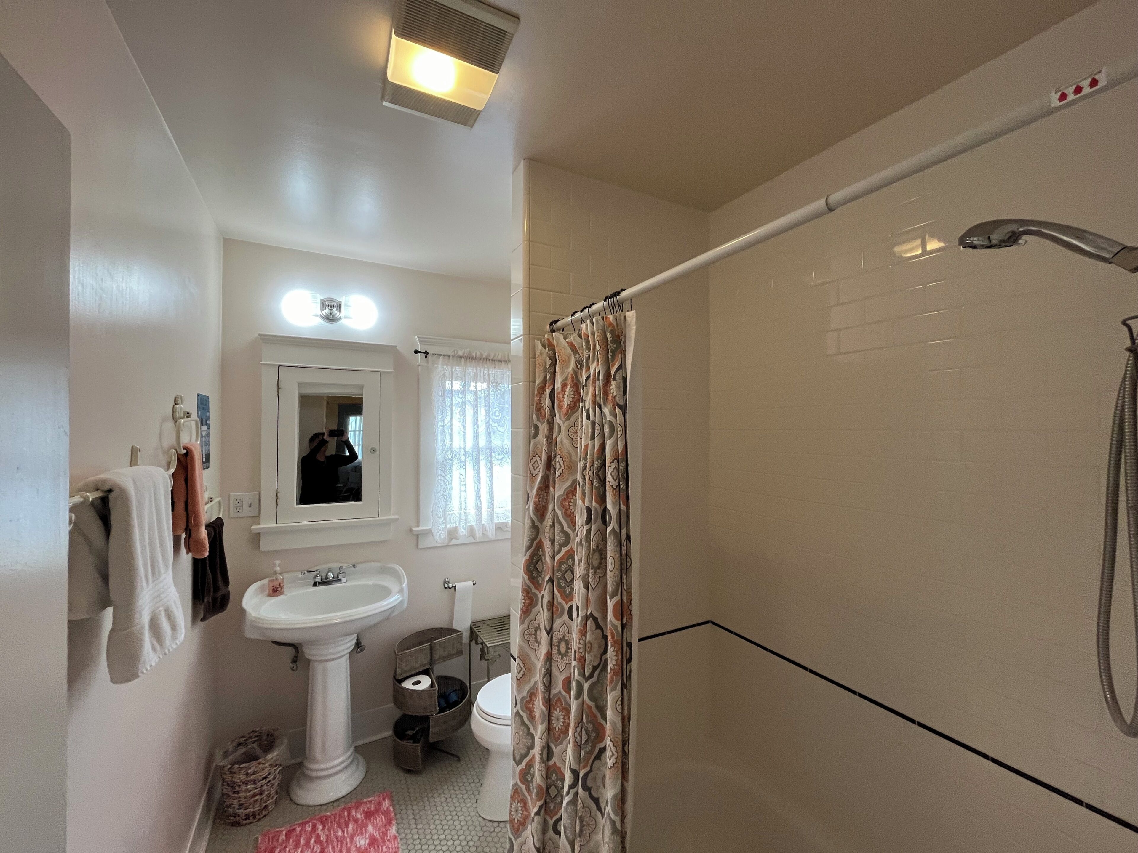 Une salle de bain avec un lavabo sur colonne, un miroir, une douche avec un rideau et des toilettes.