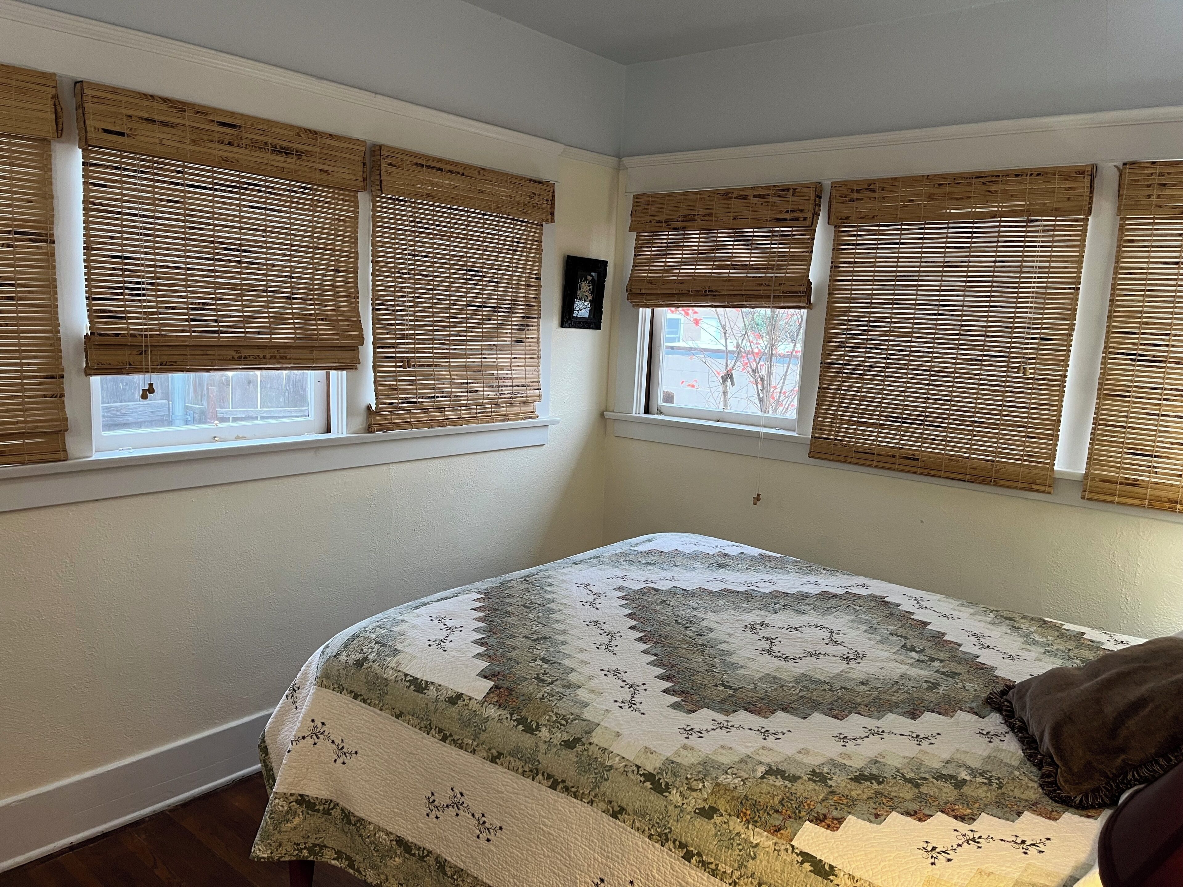 A bedroom with a bed, two windows with blinds, and a view of the outside.