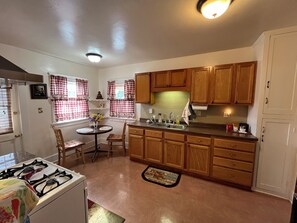 A kitchen with wooden cabinets, a gas stove, a sink, and a dining area with a table and chairs. - Cozy 1-bedroom house in peaceful Monrovia with AC. Walk to historic Myrtle Ave. (Monrovia)
