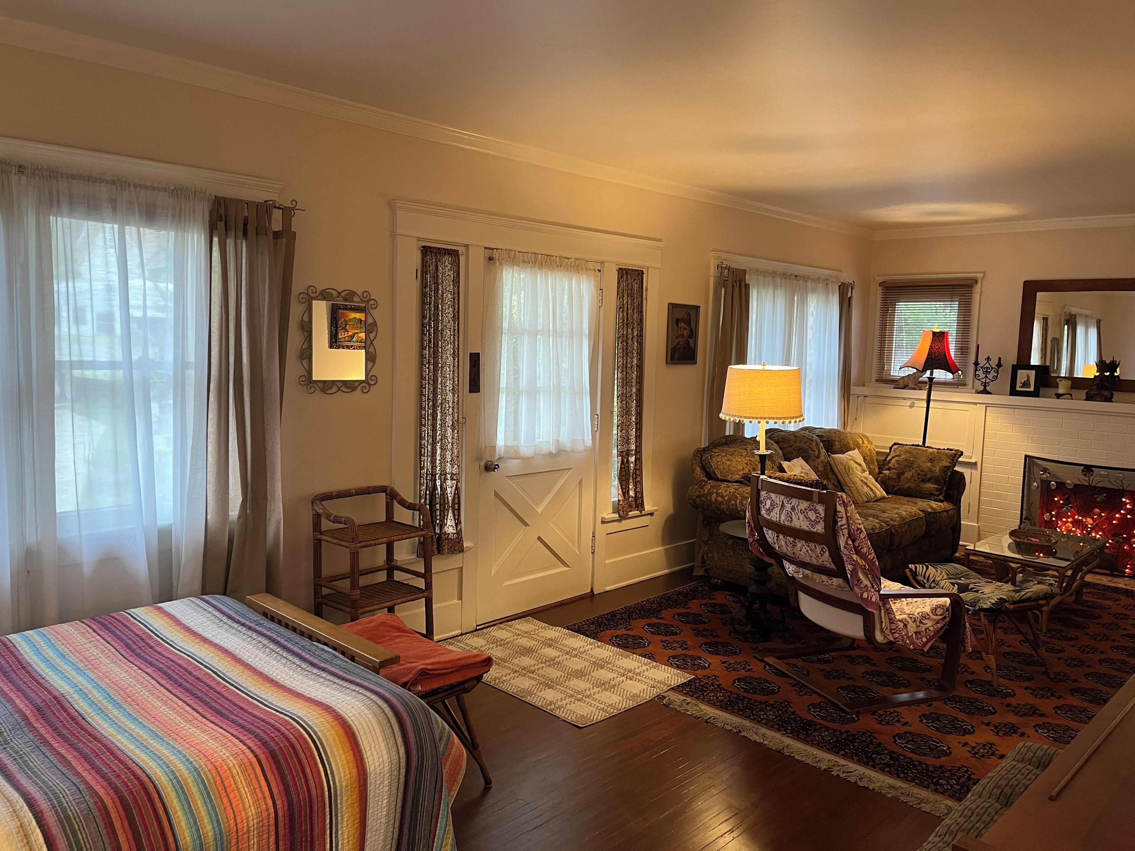 A hotel room with a bed, a sofa, a chair, a fireplace, and a window with curtains.