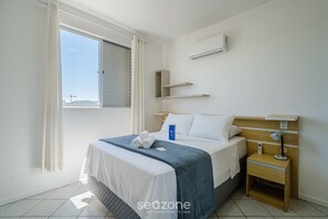 Ein Schlafzimmer mit Bett, Nachttisch, Klimaanlage und einem Vorhangfenster.